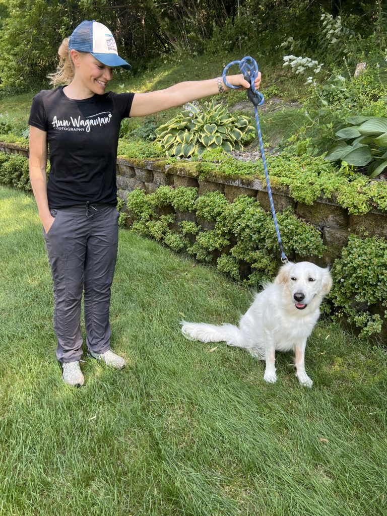 woman wearing hat holding english cream dog on a leash