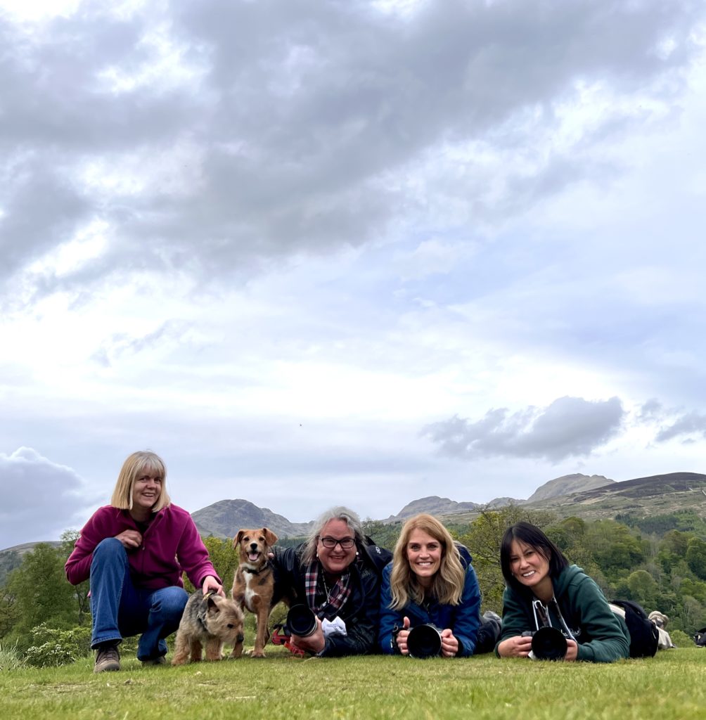 four women laying on the grass by two dogs