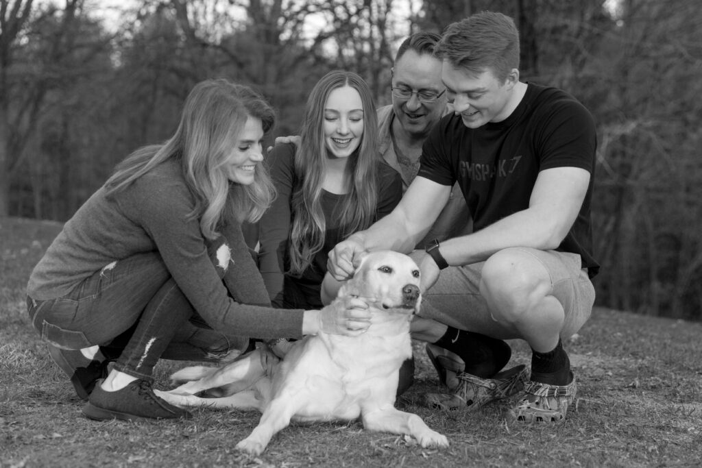 black and white image of a family petting an old yellow lab dog