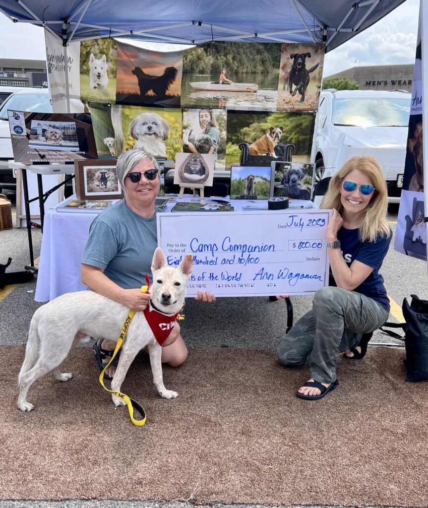 2 women and a white dog holding a large check