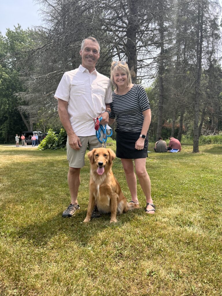 a man and woman standing outside with a golden retriever